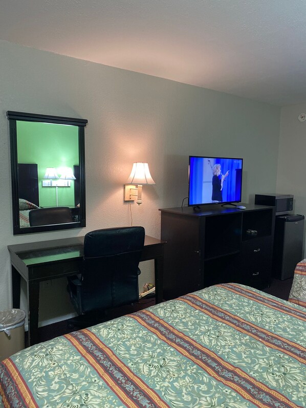 Habitación de hotel con cama, escritorio con silla, televisión, espejo y lámpara.