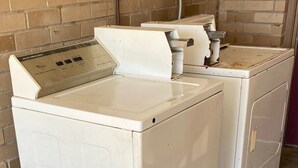A front-loading white washer and dryer unit with a control panel, placed against a brick wall in a laundry room. - Sunrise Inn (Jasper)