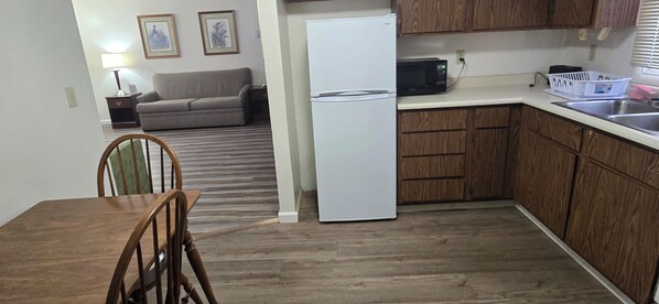 A compact kitchen with wooden cabinets, a white refrigerator, a microwave, and a dining area with a wooden table and chairs. - Red Carpet Inn Pulaski (Pulaski)