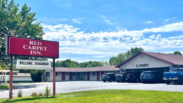 A Red Carpet Inn with a welcoming sign, a lobby, and several parked cars.