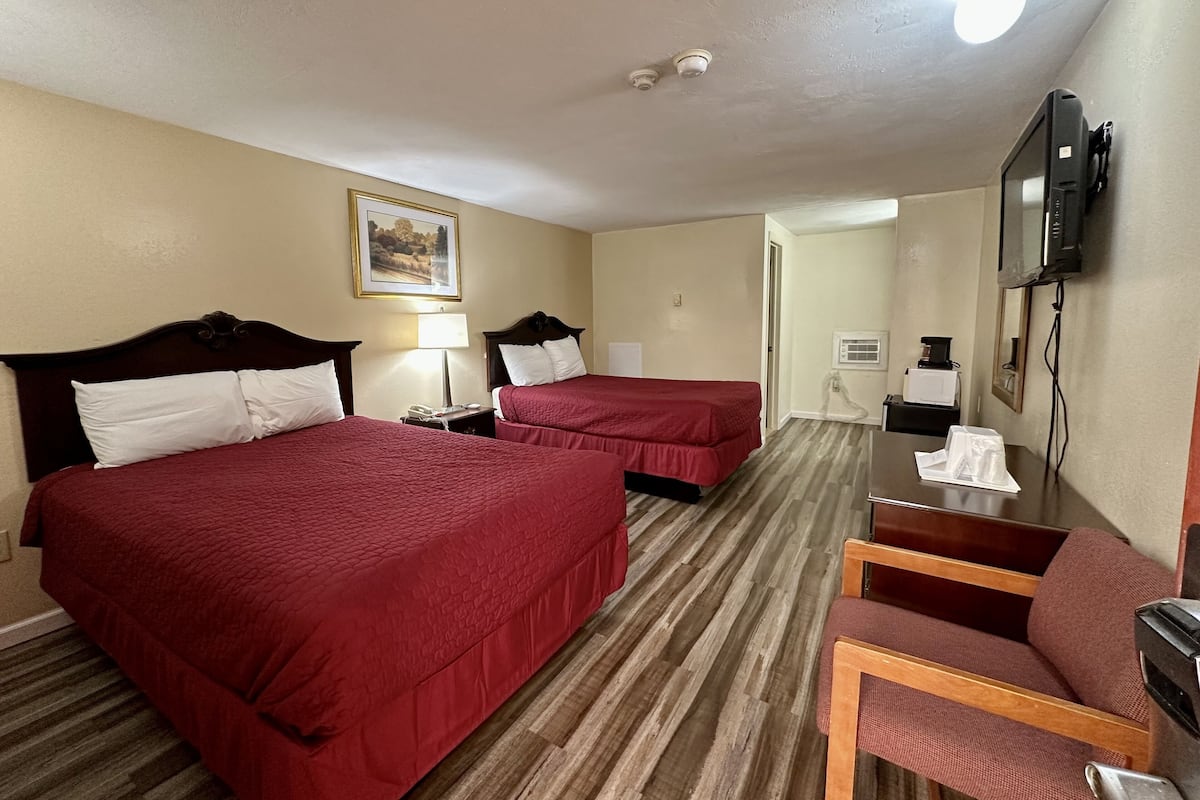 A hotel room with two beds, a desk with a chair, a television, and a painting on the wall.
