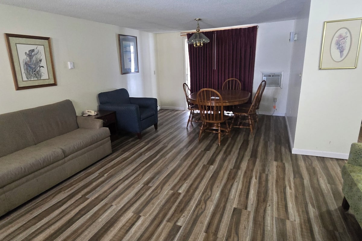 A living room with a sofa, a dining table with chairs, and a kitchen area visible through an open door.