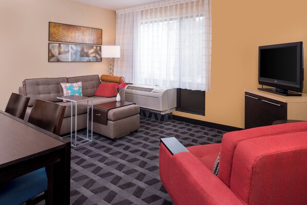 A hotel room with a sofa, a red armchair, a TV, a small table, and a lamp. - TownePlace Suites by Marriott Huntington (Huntington)