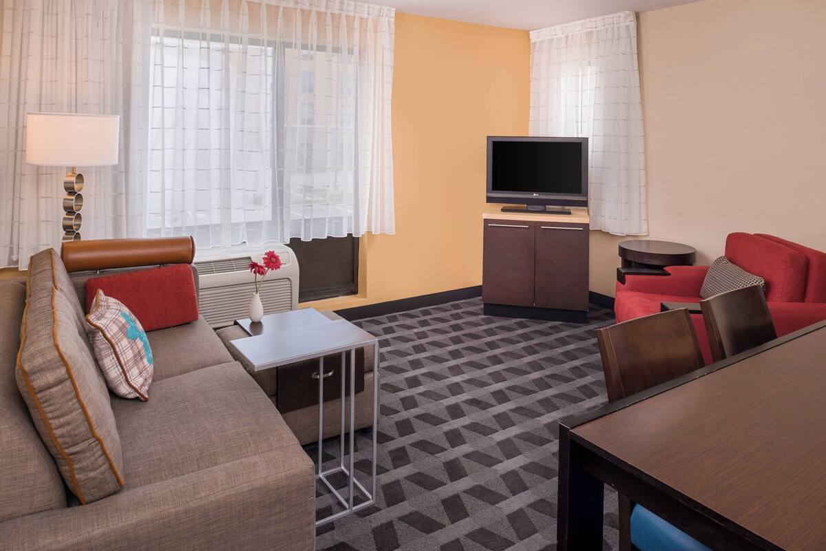 A hotel room with a sofa, a small table, a TV, and a cabinet.