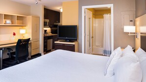 Quarto de hotel com uma cama grande, uma escrivaninha com cadeira, televisão, micro-ondas e área de chuveiro.