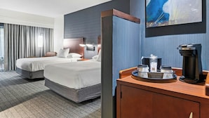 A hotel room with two beds, a coffee maker, a tray with cups and a bottle, and a painting on the wall.