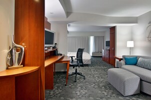 Quarto de hotel com escrivaninha, cama, sofá e televisão.