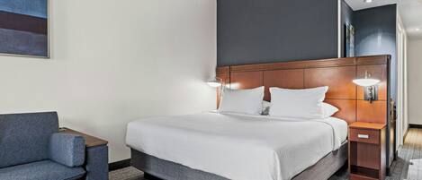 A hotel room with a bed, a chair, a nightstand, and a wall-mounted artwork.