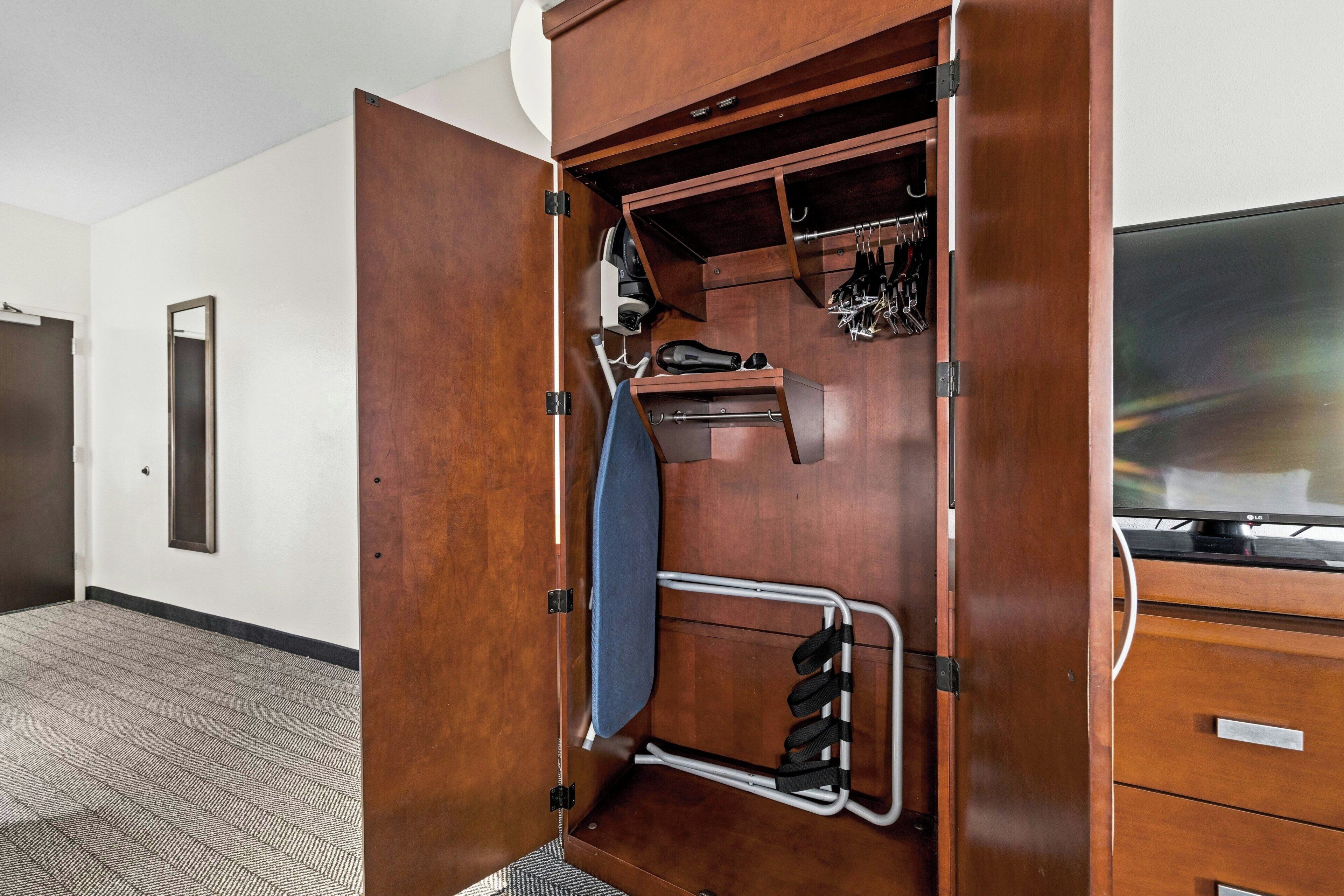 A hotel room with a wooden wardrobe, a mirror, a shoe rack, and a television.