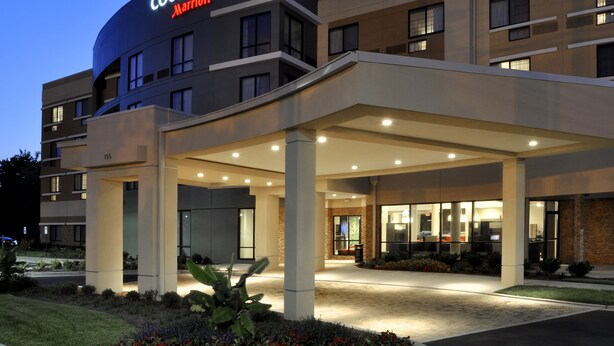 A Courtyard Marriott hotel with a modern design, featuring a covered entrance and a landscaped area with flowers.
