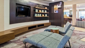 A modern living room with a flat-screen TV, built-in shelving with decorative items, and a seating area with a patterned carpet.