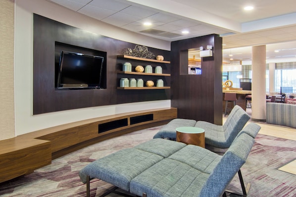 A modern living room with a flat-screen TV, built-in shelving with decorative items, and a seating area with a patterned carpet. - Courtyard by Marriott Clarksville (Clarksville)