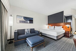Una habitación de hotel con cama, sofá, mesa de centro, lámpara, un cuadro y mesita de noche.