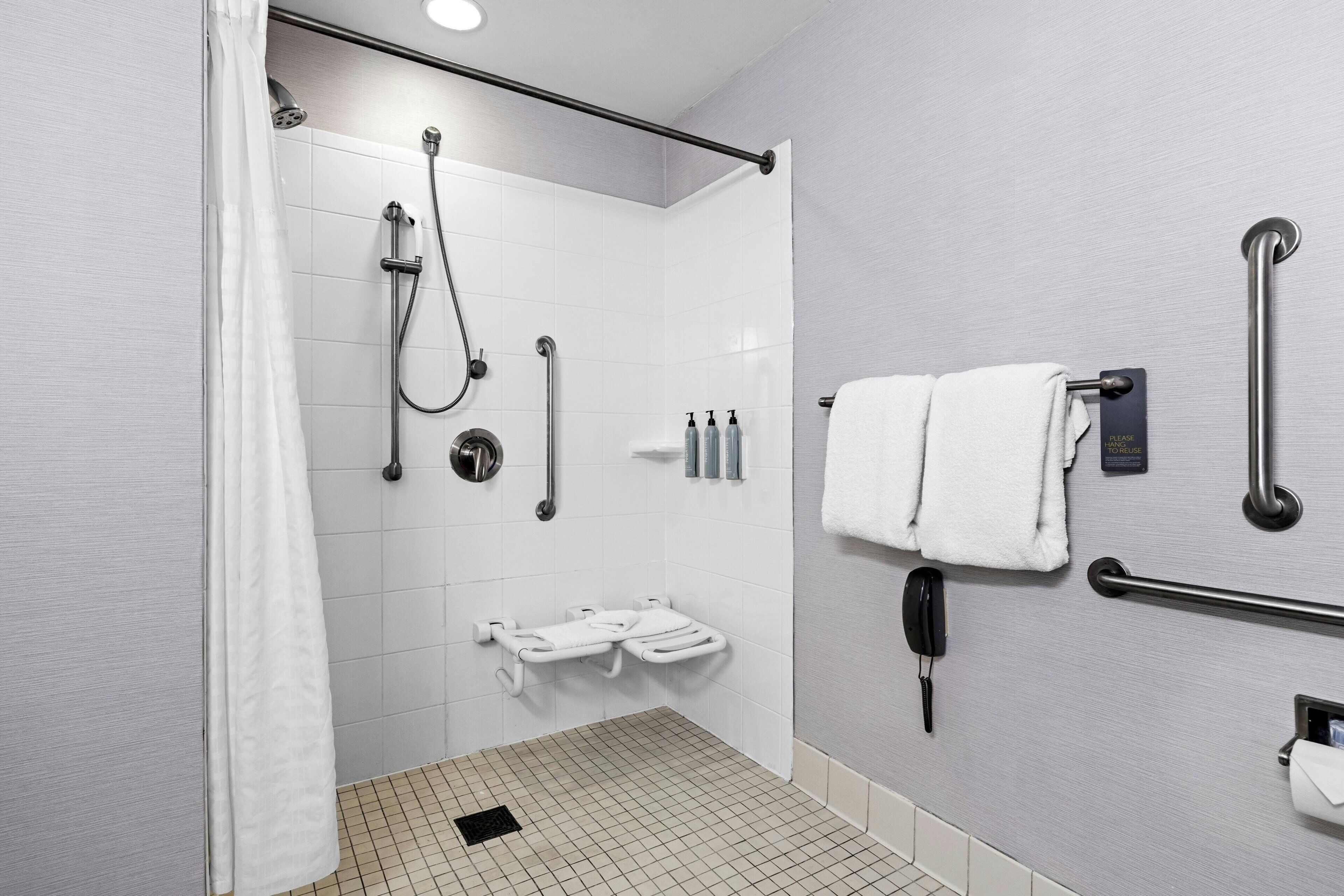 Een moderne badkamer met een douche, handgrepen, toilet en een handdoekhouder.
