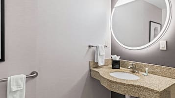 Un bany amb un lavabo de superfície de granit, un mirall rodó i un suport per a tovalloles.