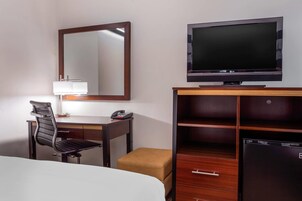 Habitación de hotel con cama, escritorio con silla, televisión, espejo, lámpara, teléfono y armario.