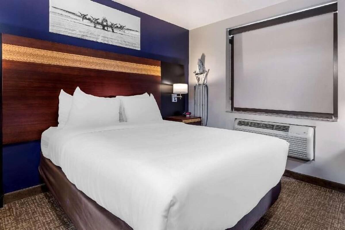 A hotel room with a large bed, a flat-screen TV, a wall-mounted heater, and a framed picture above the bed.