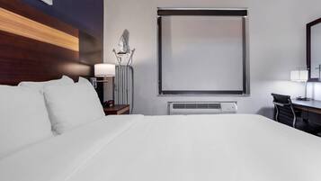Una habitación de hotel con una cama grande, un escritorio, una silla, una lámpara, un calentador y una ventana con persiana.