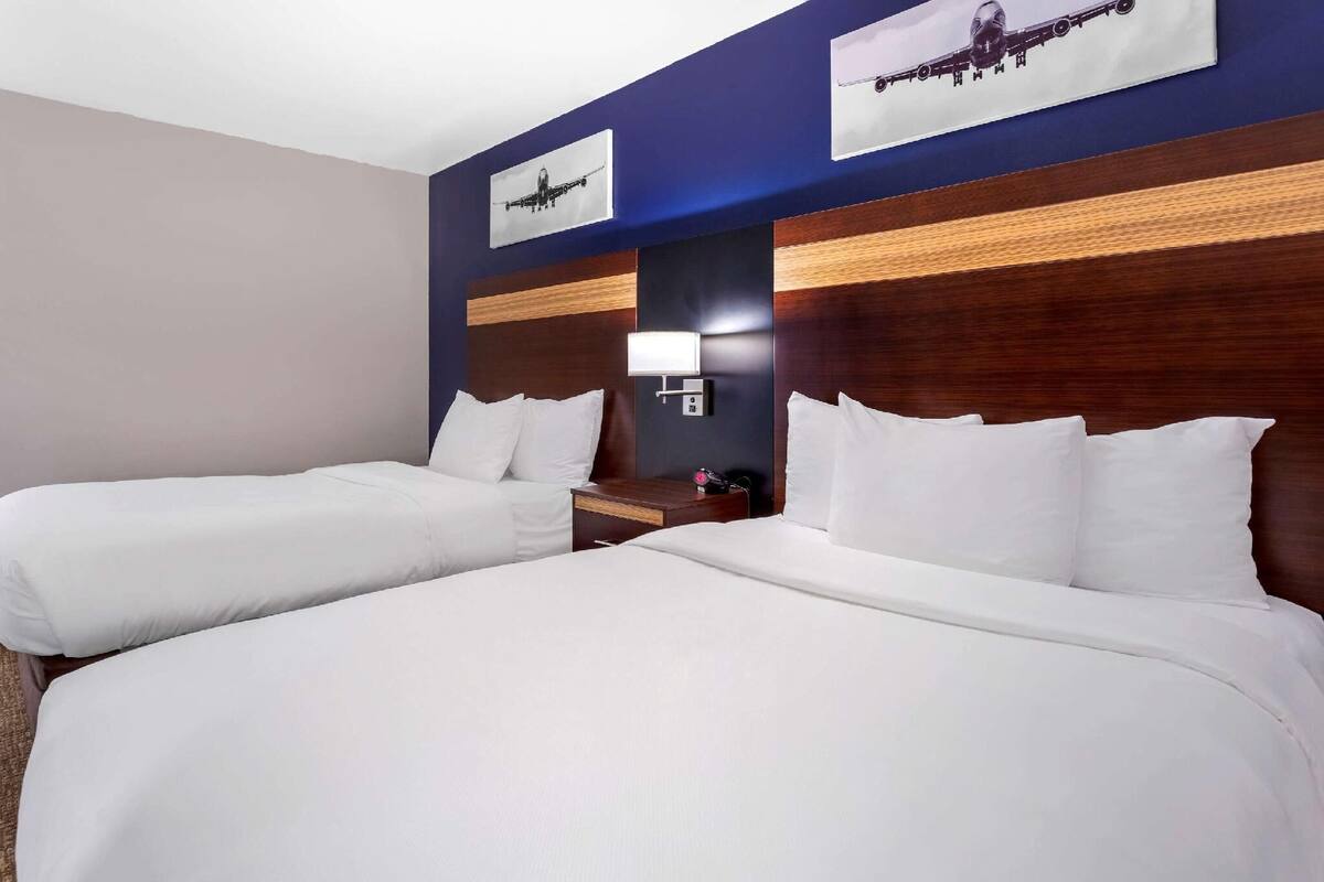 A hotel room with two beds, a nightstand, a lamp, and two airplane pictures on the wall.