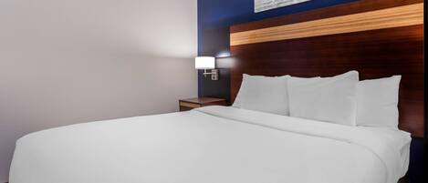 Una habitación de hotel con una cama grande, un cabecero de madera, una mesita de noche con una lámpara y una obra de arte colgada en la pared.