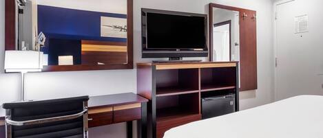 Una habitación de hotel con cama, escritorio, silla, televisor y armario.