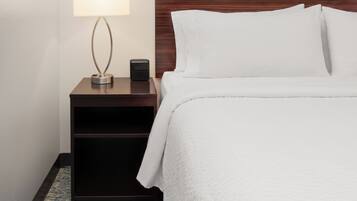 A neatly made hotel room with a bed, a bedside table with a lamp, and a small speaker.