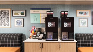 A coffee station with two espresso machines, a menu board, and various coffee-related items. - Garner Hotel Norman - University Area by IHG (Norman)