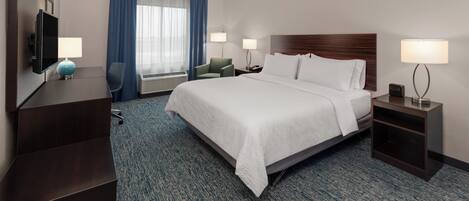 Een hotelkamer met een bed, een bureau, een stoel, een televisie en een raam met gordijnen.