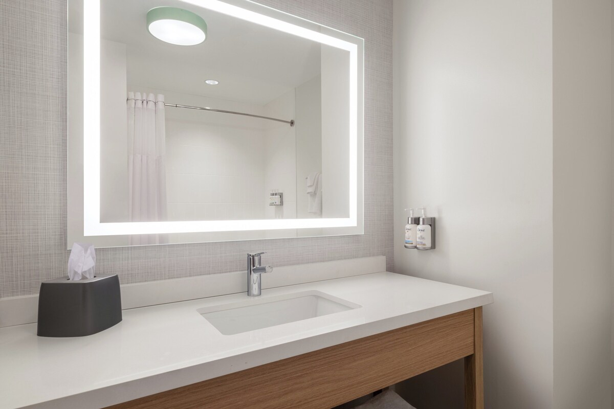 A modern bathroom with a large mirror, a white sink, a towel rack, and a shower curtain.