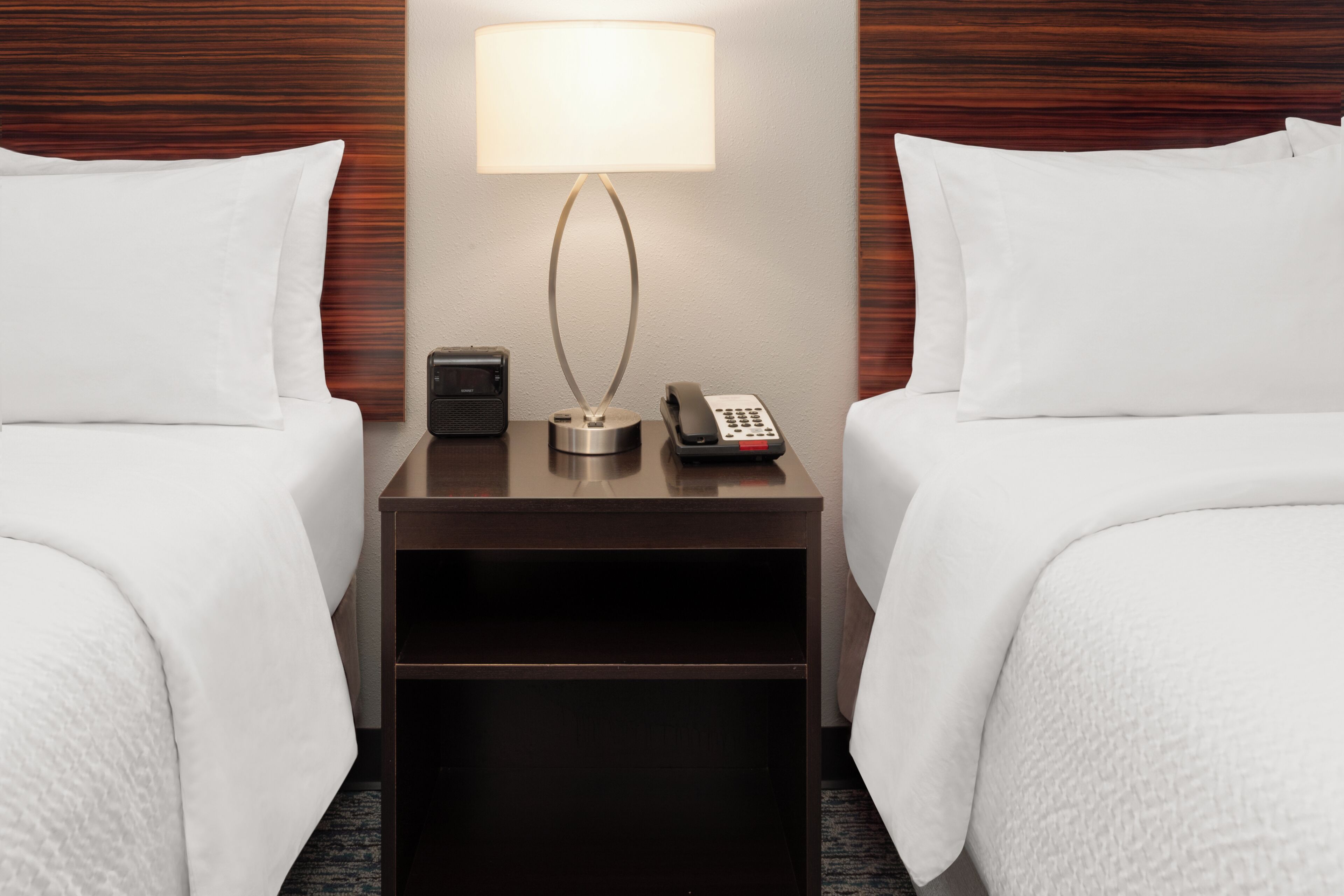 Habitación de hotel con dos camas, una mesita de noche, una lámpara, un teléfono y un control remoto.