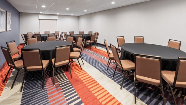 A conference room with a large oval table, multiple chairs, and a projector screen. - Garner Hotel Norman - University Area by IHG (Norman)