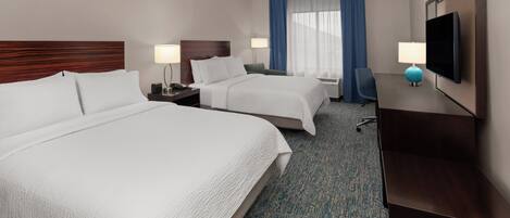 A hotel room with two beds, a desk, a TV, and a window with curtains.