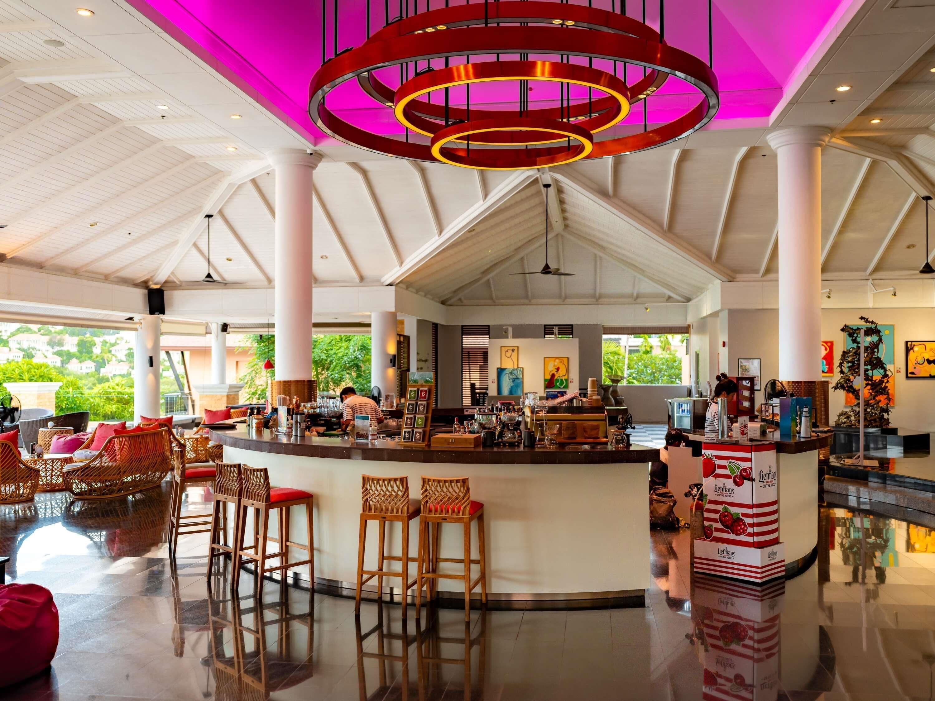 A spacious lobby with a central bar, high ceilings, and large windows offering views of greenery.