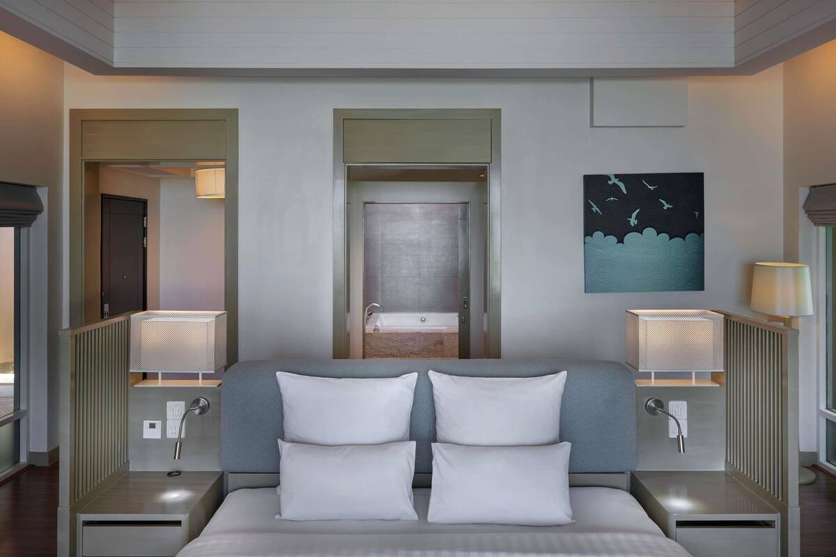 Een moderne hotelkamer met een groot bed, twee nachtkastjes met lampen, een bijzettafeltje, een schilderij aan de muur en uitzicht op de badkamer door een deur.