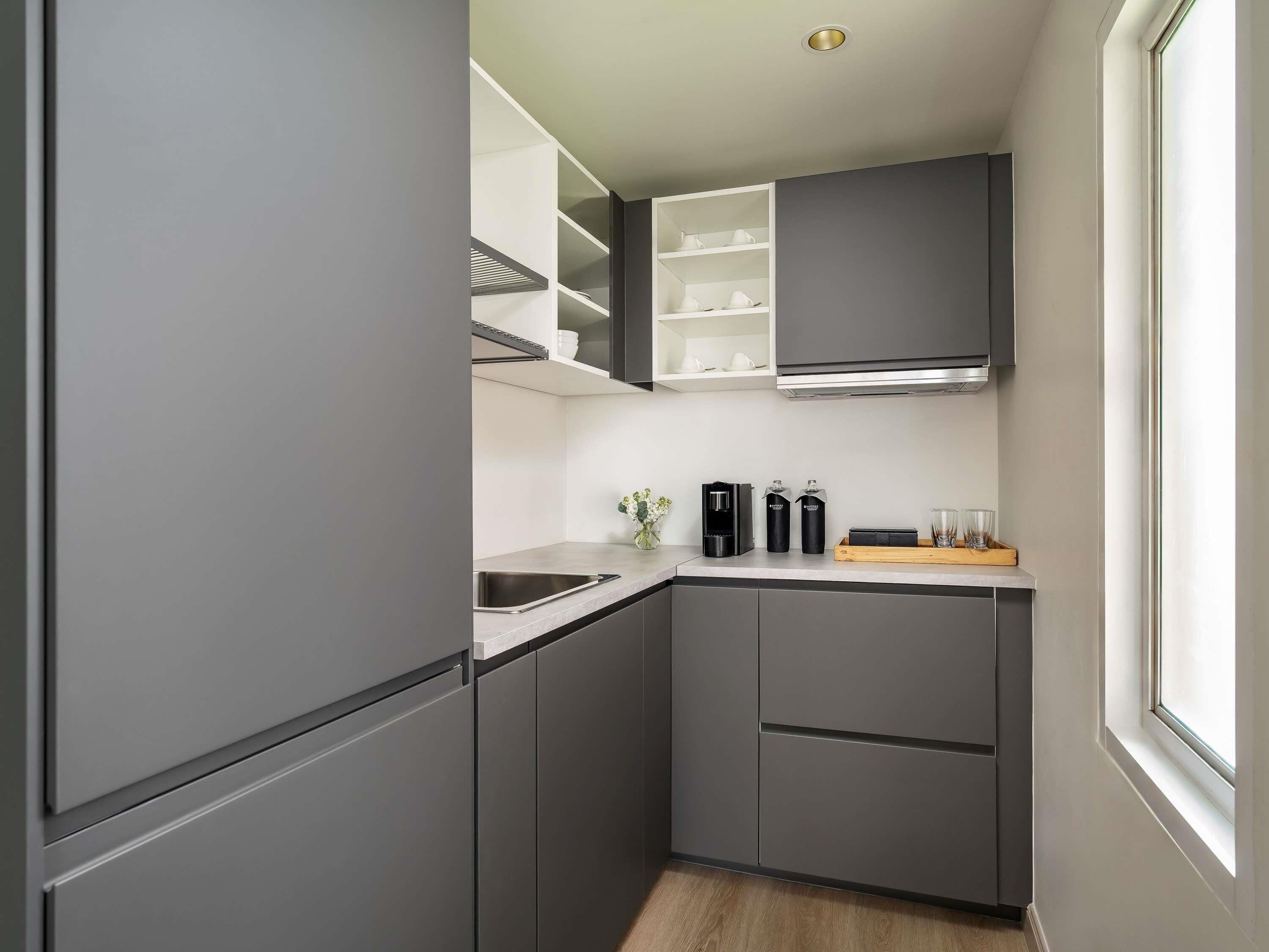 Een moderne keuken met grijze keukenkastjes, een roestvrijstalen spoelbak en een raam dat voor natuurlijk licht zorgt.