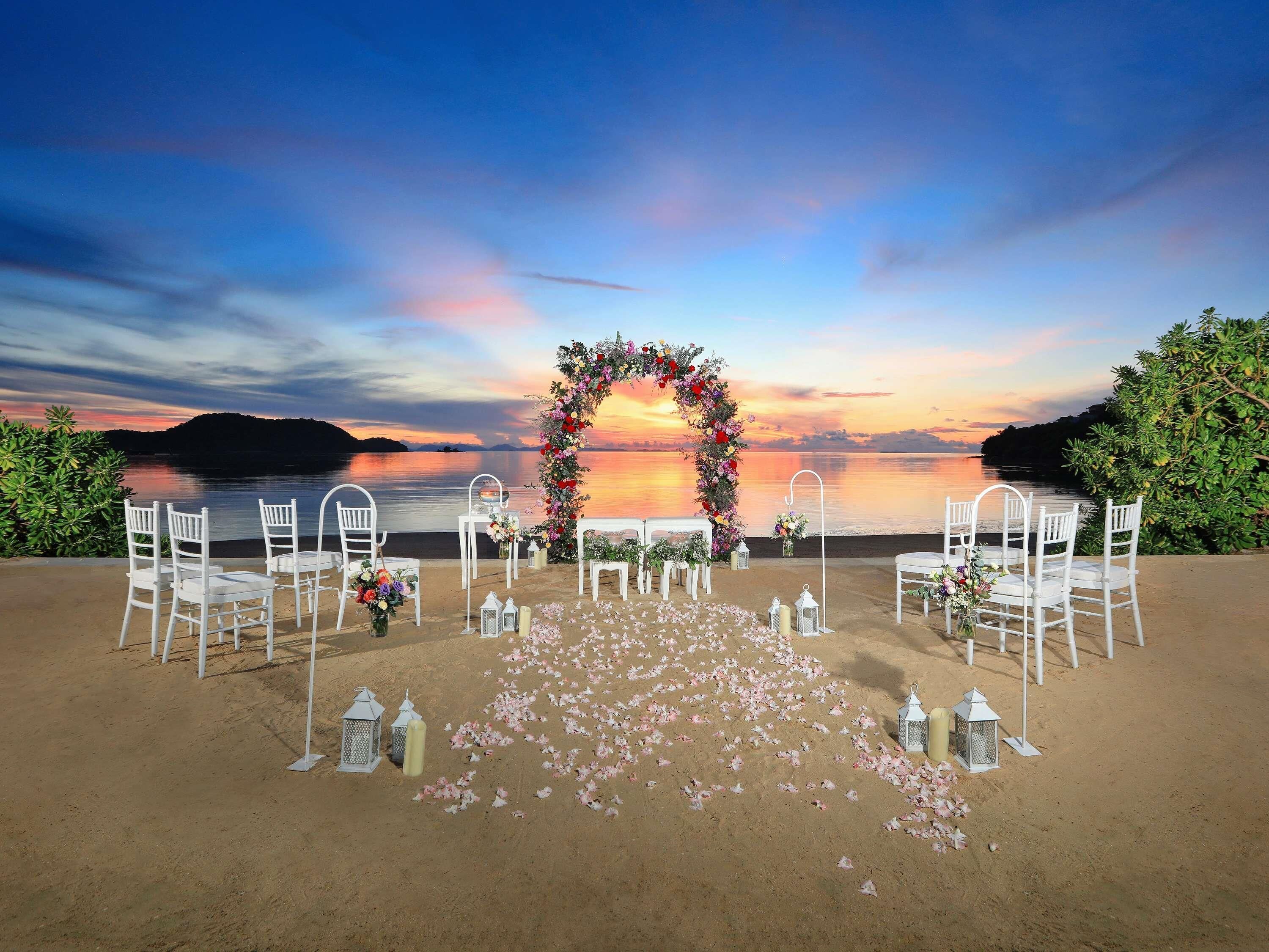 A beach wedding setup with a floral arch and white chairs.