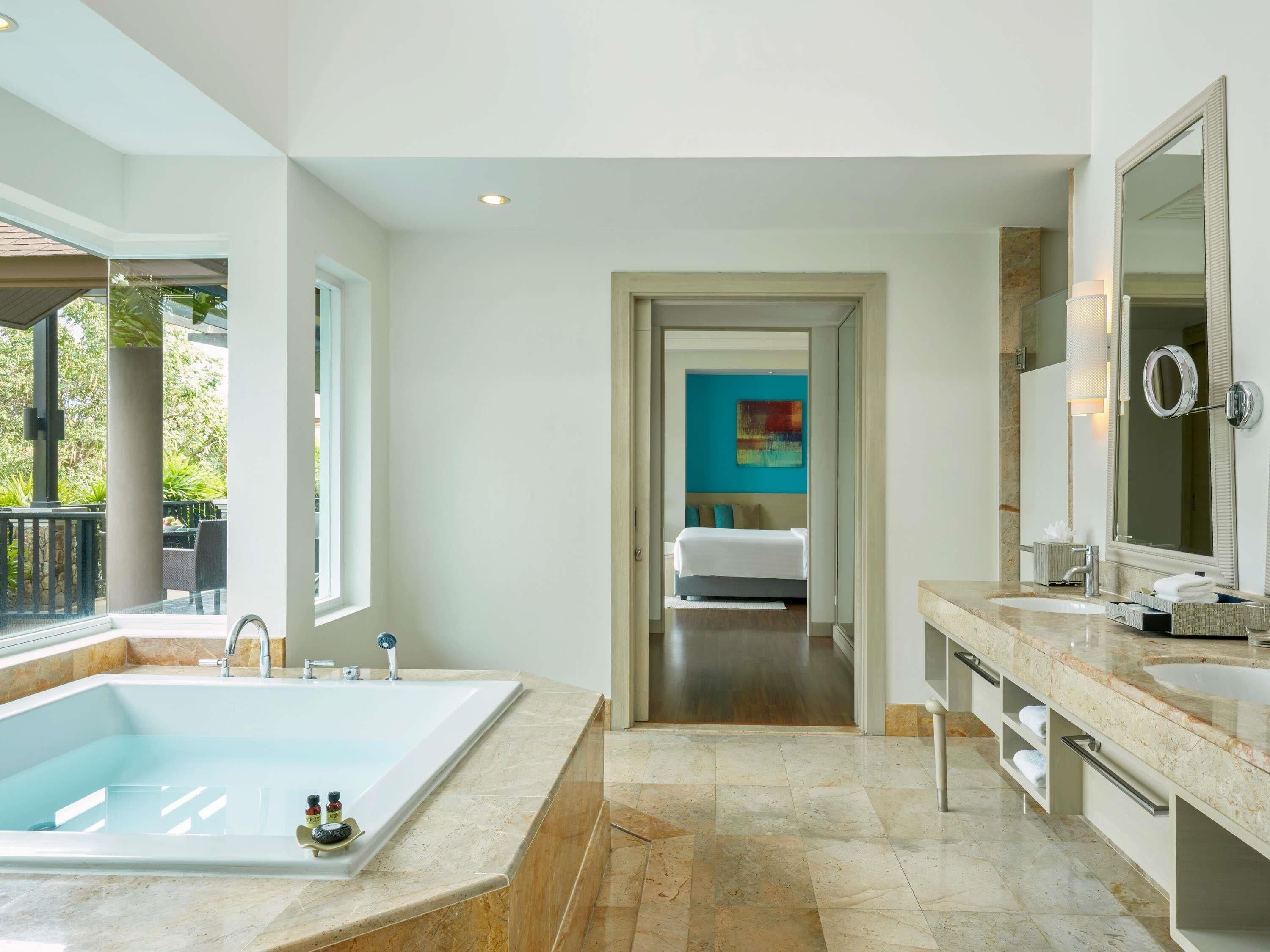 Une salle de bain moderne dotée d’une grande baignoire, d’une douche à l’italienne et d’une chambre séparée, visible à travers une porte ouverte.