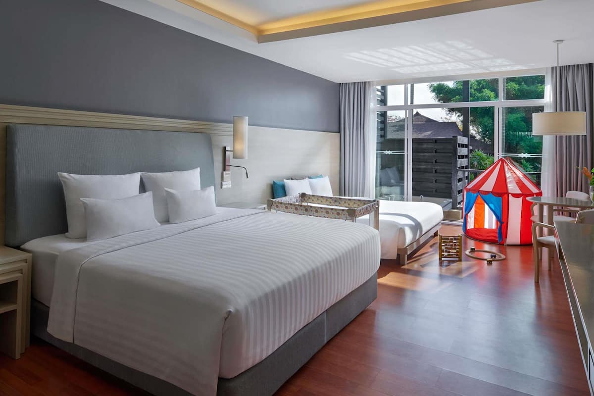 Een moderne hotelkamer met een groot bed, een klein bureau, een raam met gordijnen en een kinderspeeltent.