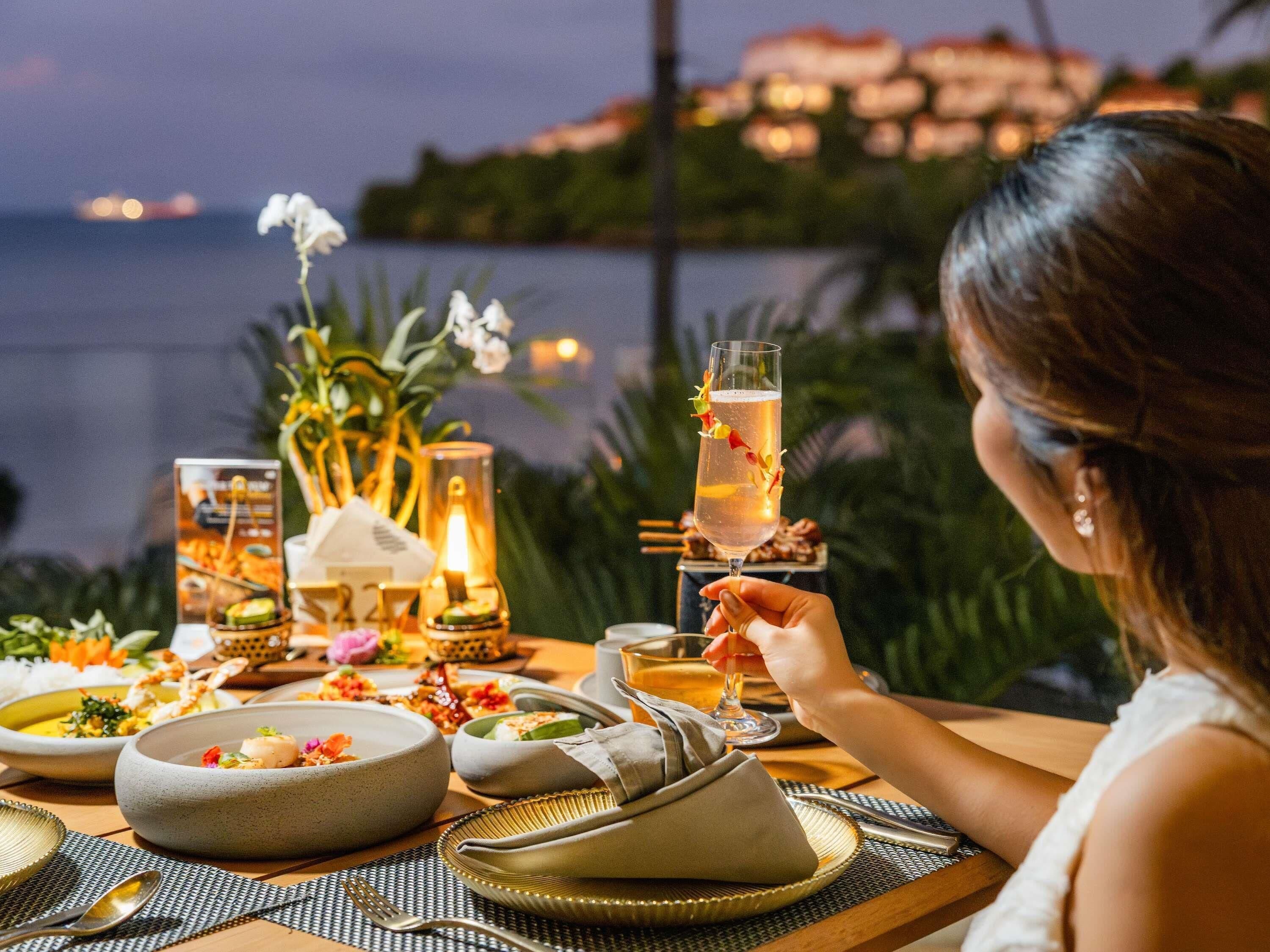 Une table dressée avec de la vaisselle, un verre rempli d’une boisson et une vue sur la mer.