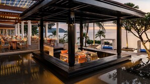 An outdoor dining area with tables and chairs, a covered seating area, and a view of the sea. - Pullman Phuket Panwa Beach Resort (Wichit)