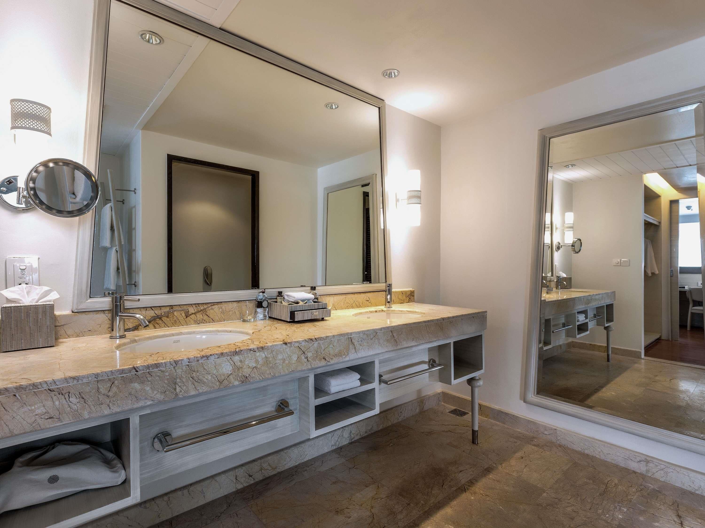 A bathroom with a large mirror, two sinks, a towel rack, and a storage cabinet.