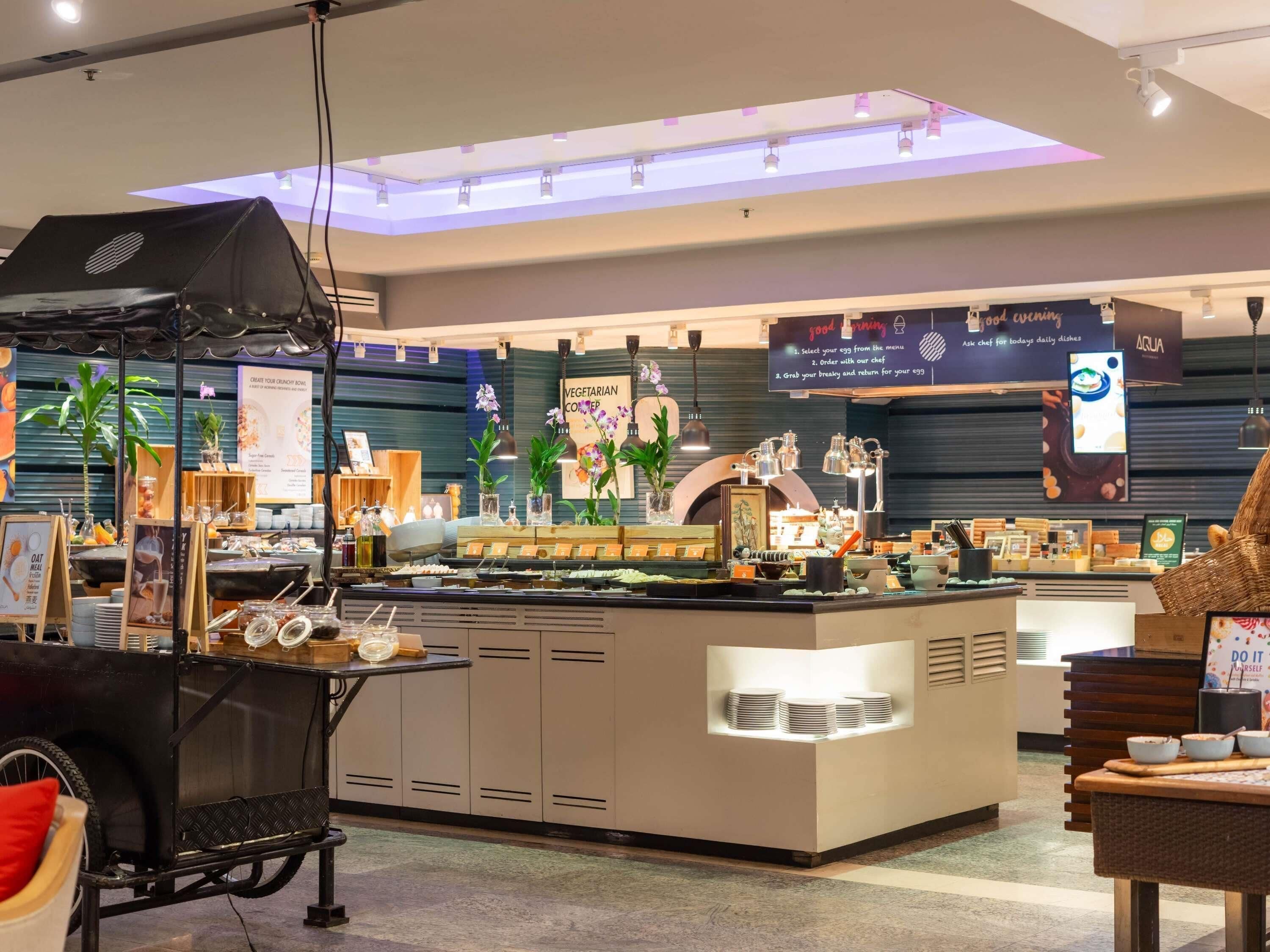 A buffet area with a central island, various food stations, and a sign indicating vegetarian options.
