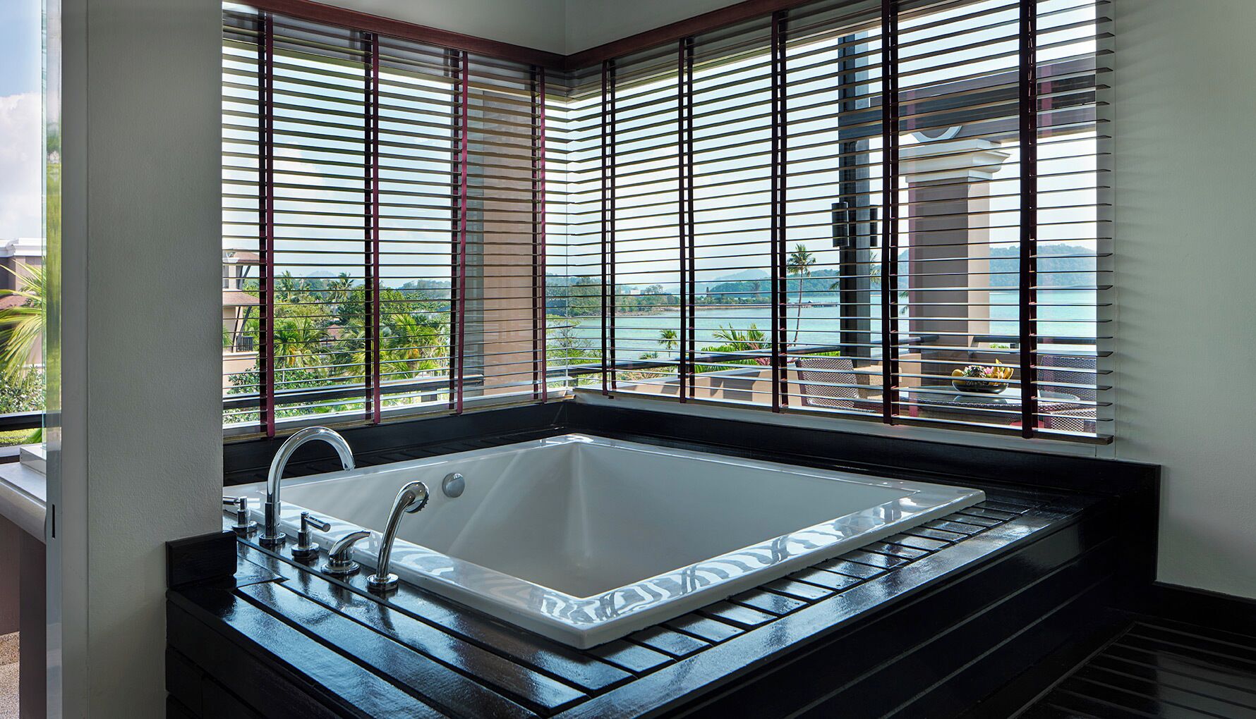 Un baño moderno con una bañera grande, un lavamanos y vistas al exterior a través de amplias ventanas.