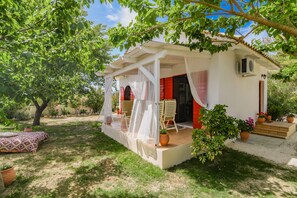A white house with a covered porch, a red door, and a small garden with potted plants. - Villas Therianos (Zakynthos)