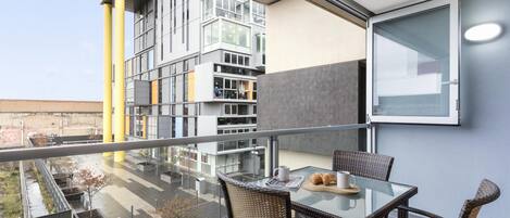 A modern balcony with a glass table, wicker chairs, and a view of a cityscape.
