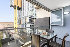 A modern balcony with a glass table, wicker chairs, and a view of a cityscape.