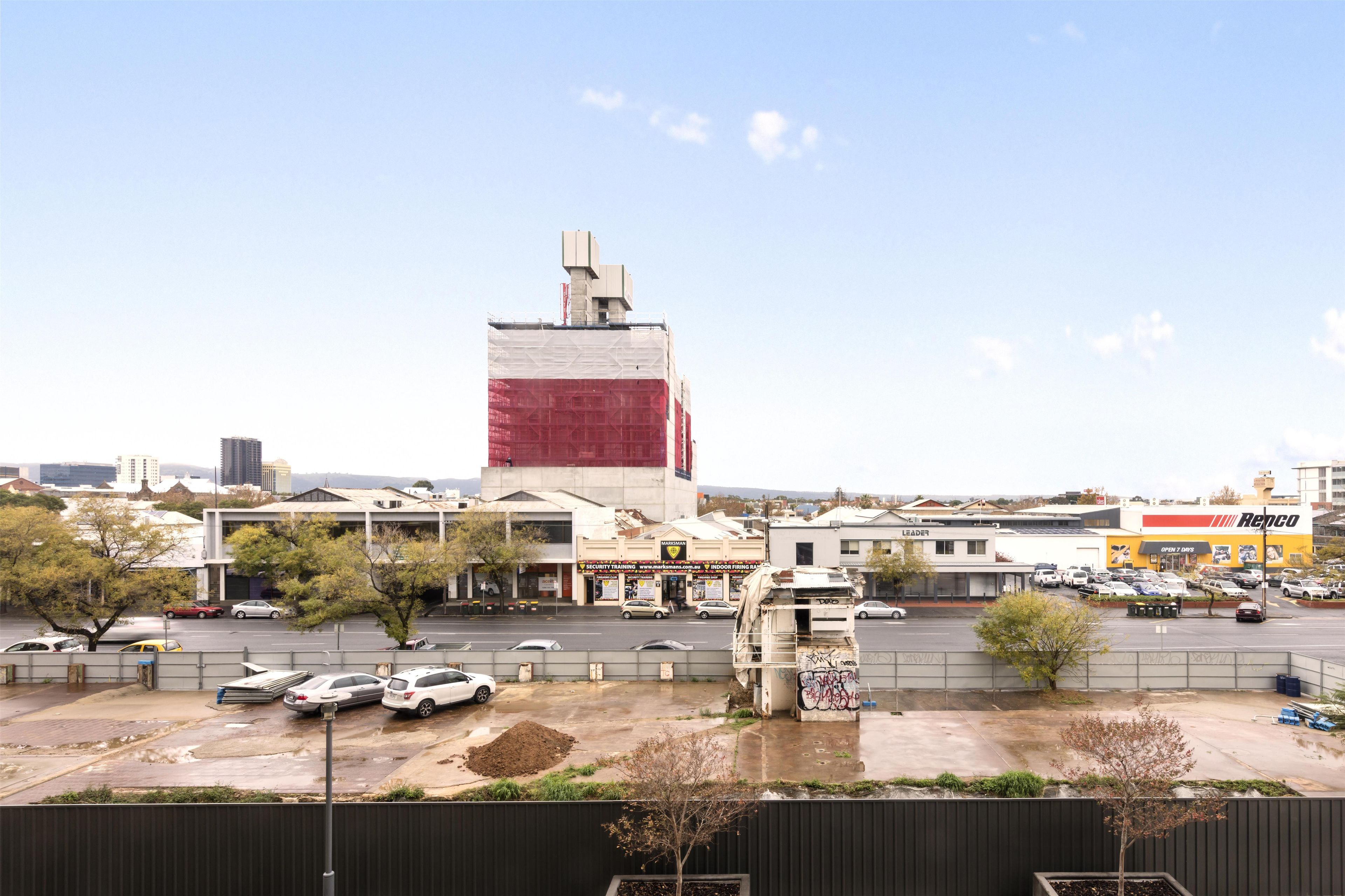 A parking lot with several cars, a building with a red and white facade, and a clear sky.