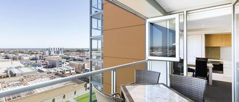 A balcony with a view of the city, wicker furniture, and a glass door leading to a kitchen area.
