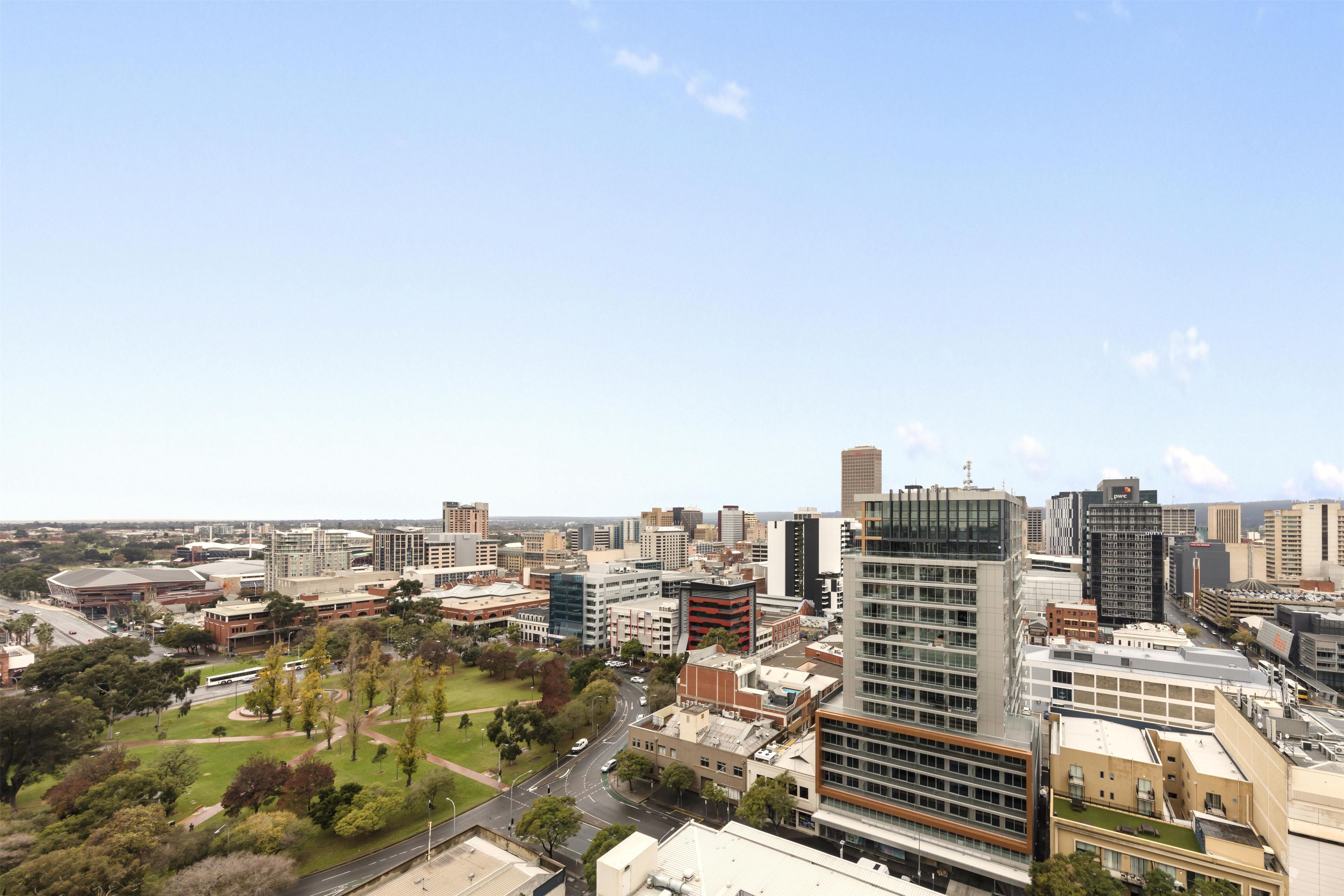 A cityscape with modern buildings, a park area, and a clear sky.