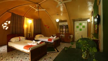 A cozy, compact room with a bed, two chairs, a small table, and a ceiling fan.